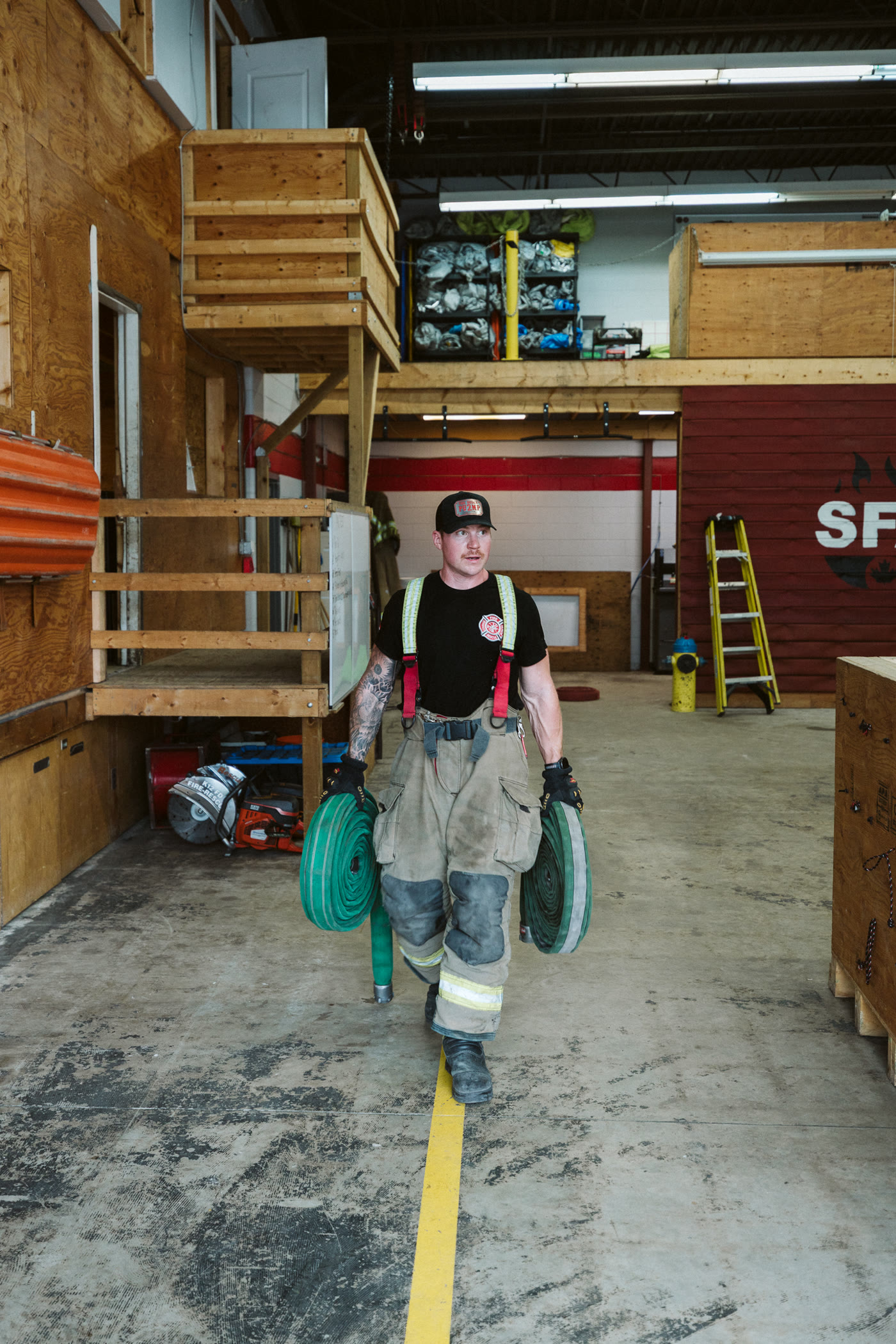 Firefighter carrying two hose rolls through the apparatus bay.