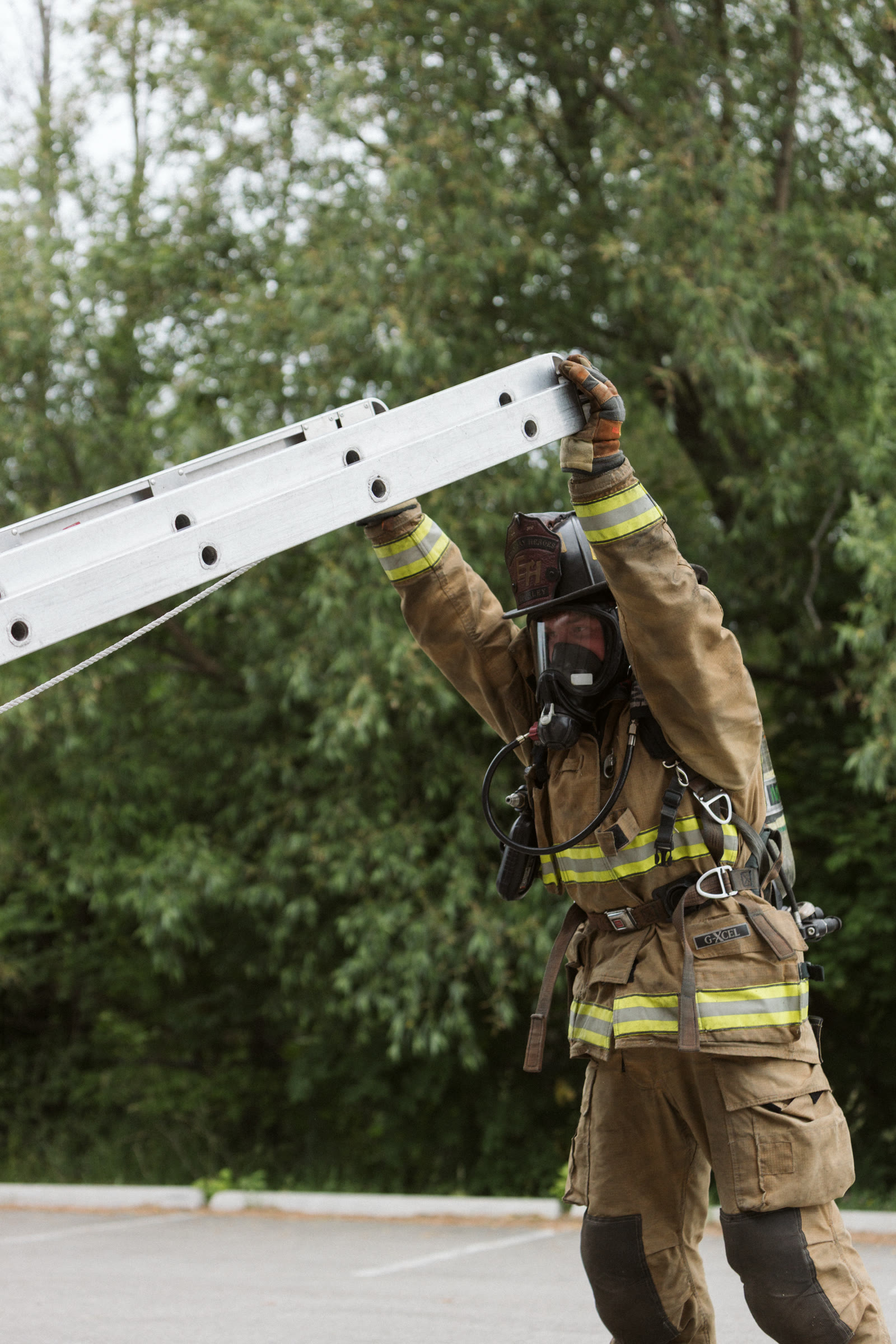 Firefighter in full gear raising an extension ladder overhead.